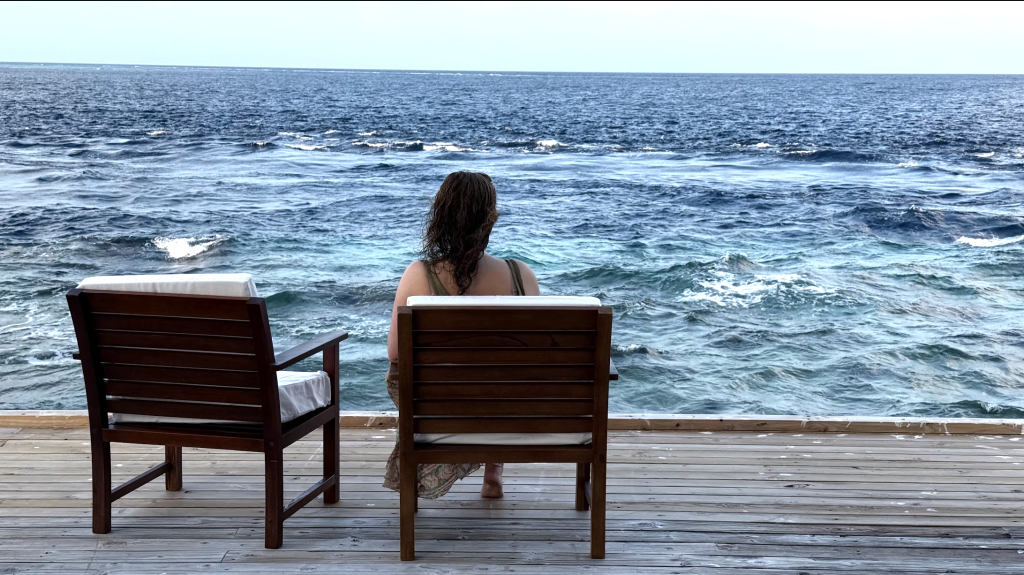 A woman sits in a chair, gazing at the ocean waves, capturing a peaceful moment.
