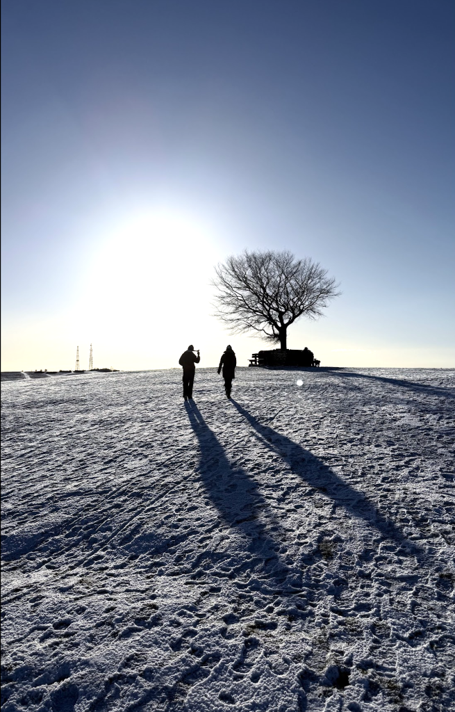 Two figures walk across a snowy landscape towards a silhouetted tree at sunrise.